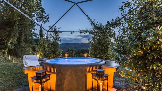 Een hottub met twee stoelen en een tafel, omgeven door bomen en uitzicht op heuvels.
