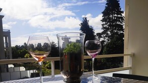 Un balcón con una mesa de vidrio, dos copas de vino y un florero con una planta.