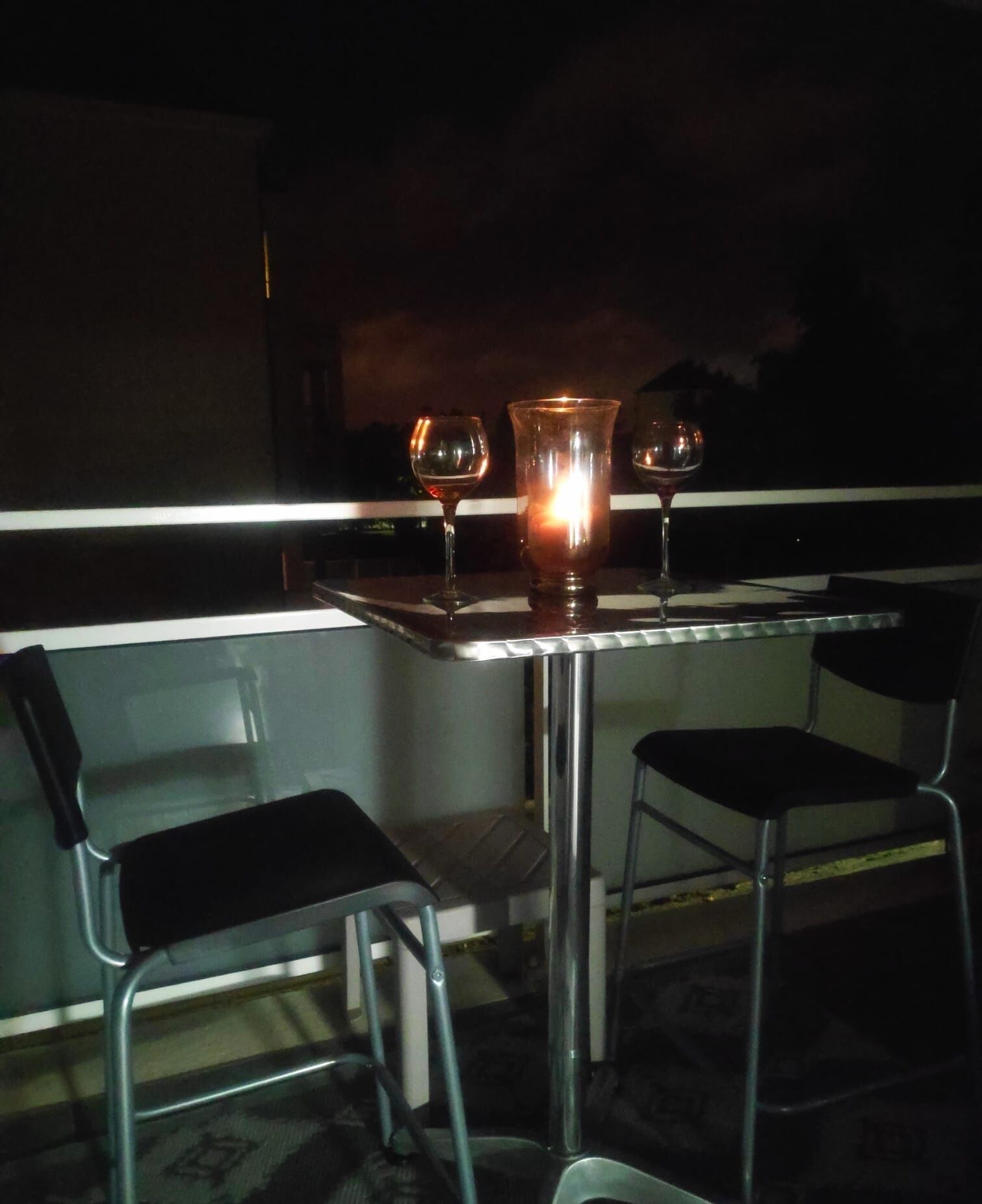 Una pequeña mesa con dos sillas, una vela y dos copas de vino.