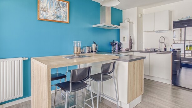 Una cocina moderna con una pared de acento azul, una isla de madera con taburetes de bar y una campana extractora de acero inoxidable.