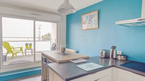 Una cocina moderna con una pared azul de acento, un comedor con mesa y sillas, y vistas al balcón exterior.