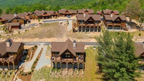 Un resort con varias cabañas de madera, un camino central y vistas de las colinas boscosas circundantes.