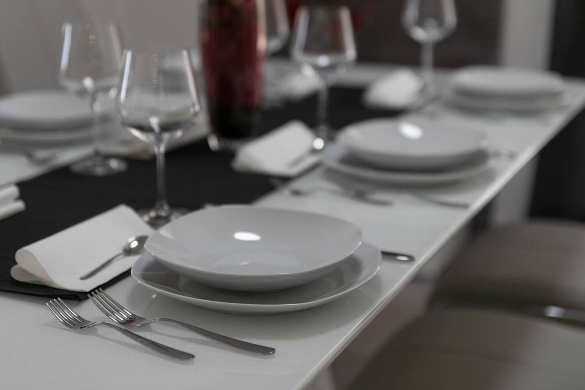 A neatly set dining table with white plates, forks, and wine glasses.