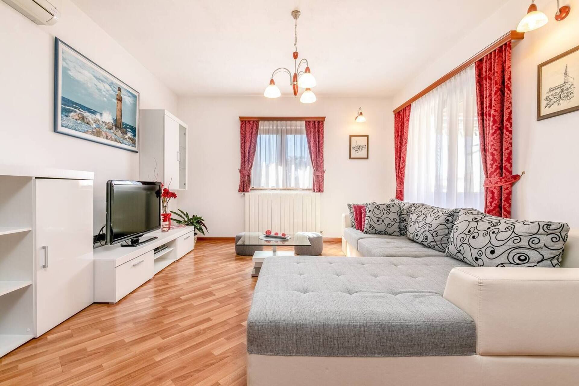 A modern living room with a flat-screen TV, a grey sofa, and a coffee table.