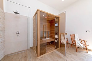 A modern bathroom with a glass shower enclosure, wooden flooring, and a wooden bath area.