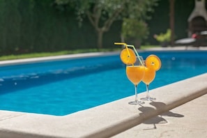 A swimming pool with two glasses of orange juice on the edge.