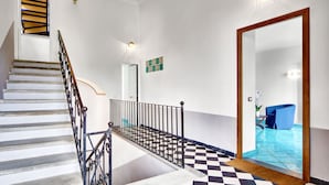 Una escalera con barandilla de metal negro, piso a cuadros y una silla azul al fondo.