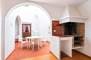 Une cuisine avec un four en briques, des murs blancs et un coin repas comprenant une table et des chaises.