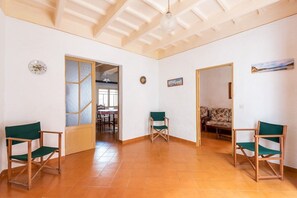 Une pièce spacieuse avec un plafond haut, un sol carrelé et deux fauteuils verts. Des portes donnent accès à d’autres pièces, et une horloge est accrochée au mur.