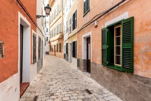 A narrow cobblestone street flanked by buildings with traditional shutters and a classic European architectural style.