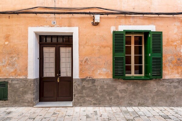 A building facade with a brown door and green shutters, a number '31' sign, and a cobblestone ground.