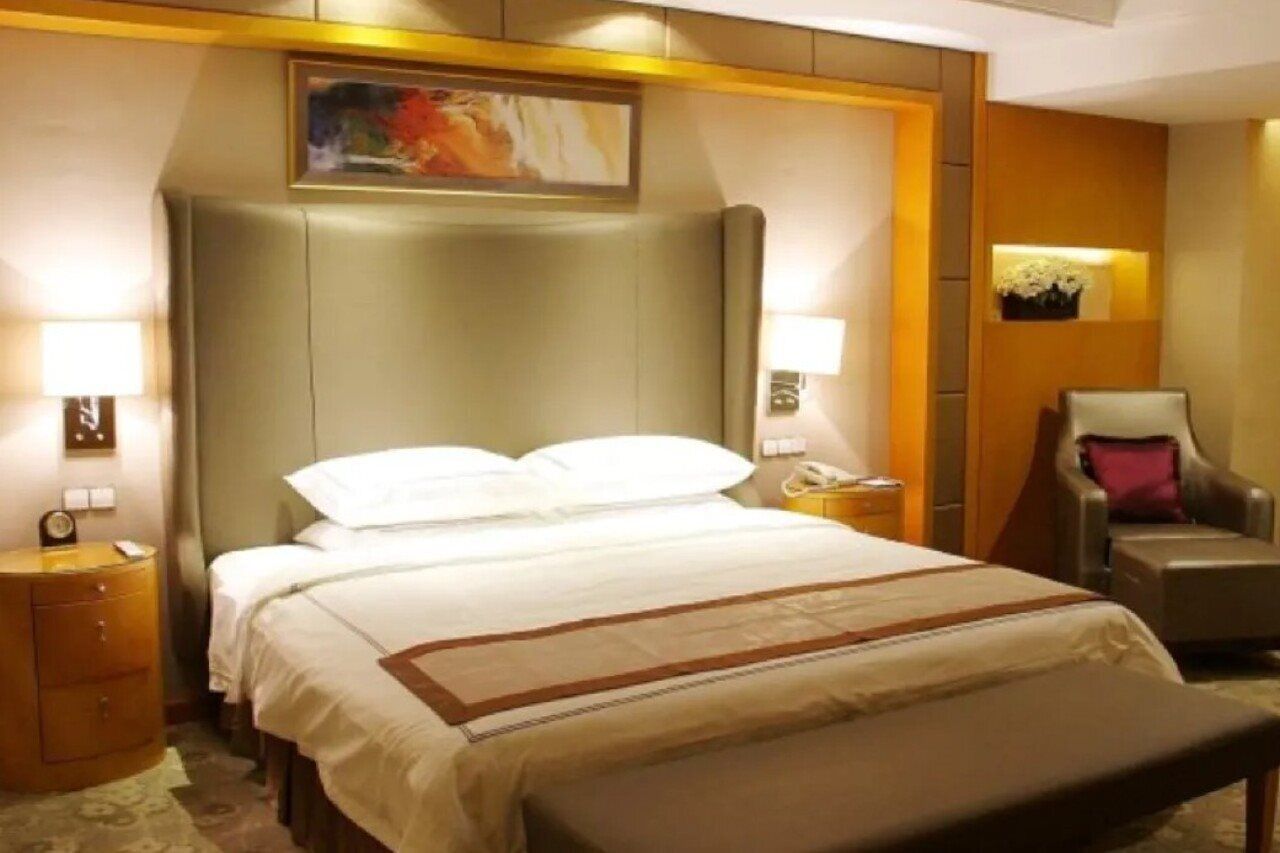A hotel room with a large bed, a bedside table with a lamp, a chair, and a painting on the wall.