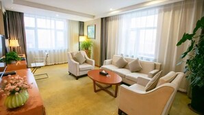A hotel room with a sofa set, a coffee table, a desk with a lamp, and a large window with curtains. - Boyue Hotel (Changchun)