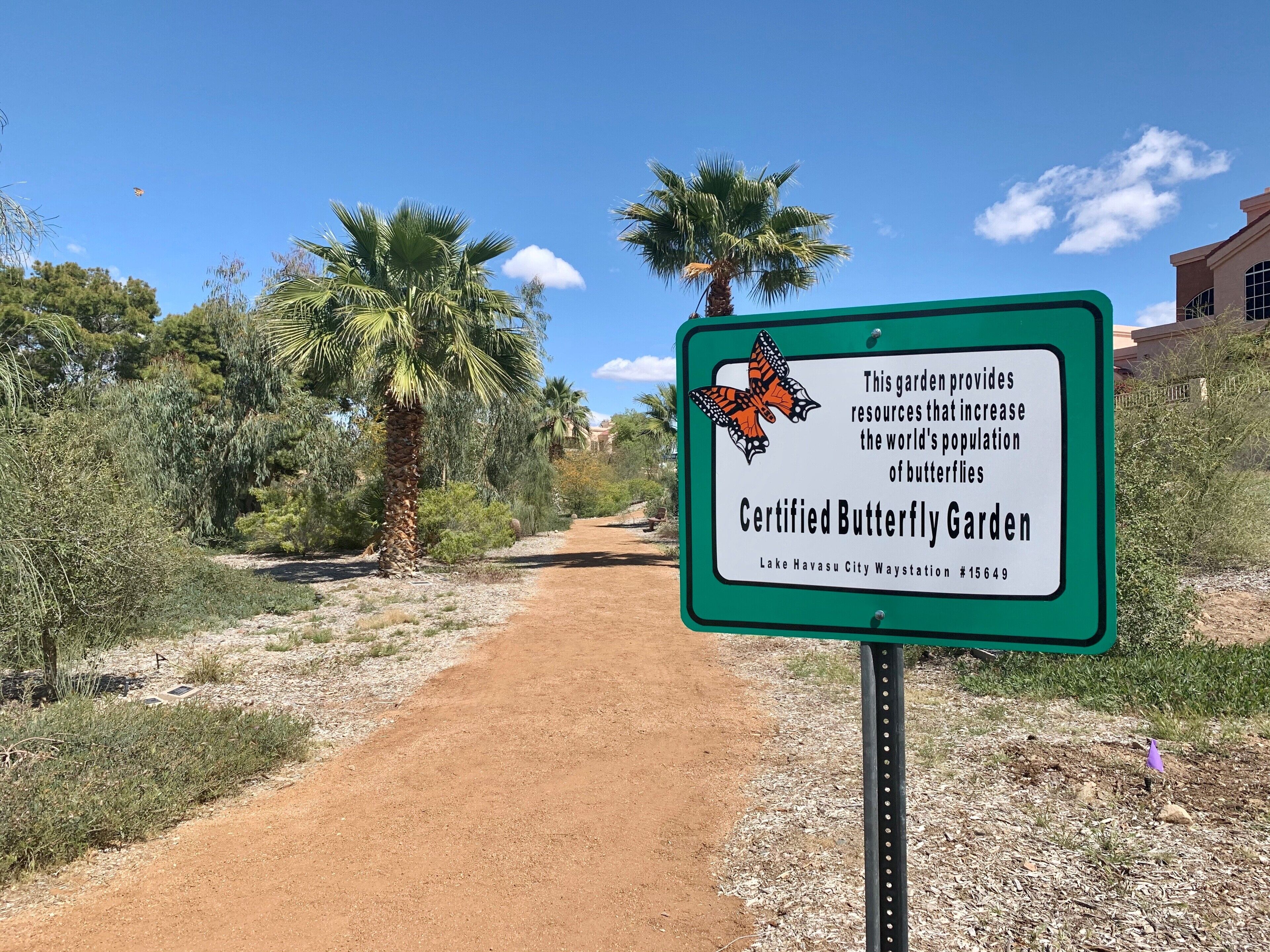 A dirt path leading through a garden with a sign indicating it is a Certified Butterfly Garden.