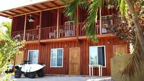 A two-story wooden building with a balcony, a white ATV parked in front, and a small table on the ground floor.