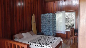 A wooden room with a bed, a surfboard, and a window with curtains.