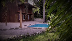 A wooden house with a swimming pool surrounded by a stone border and greenery.