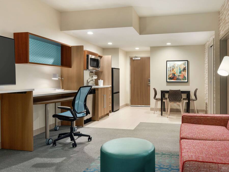 A modern hotel room with a kitchenette, a desk, a comfortable seating area, and a dining table.