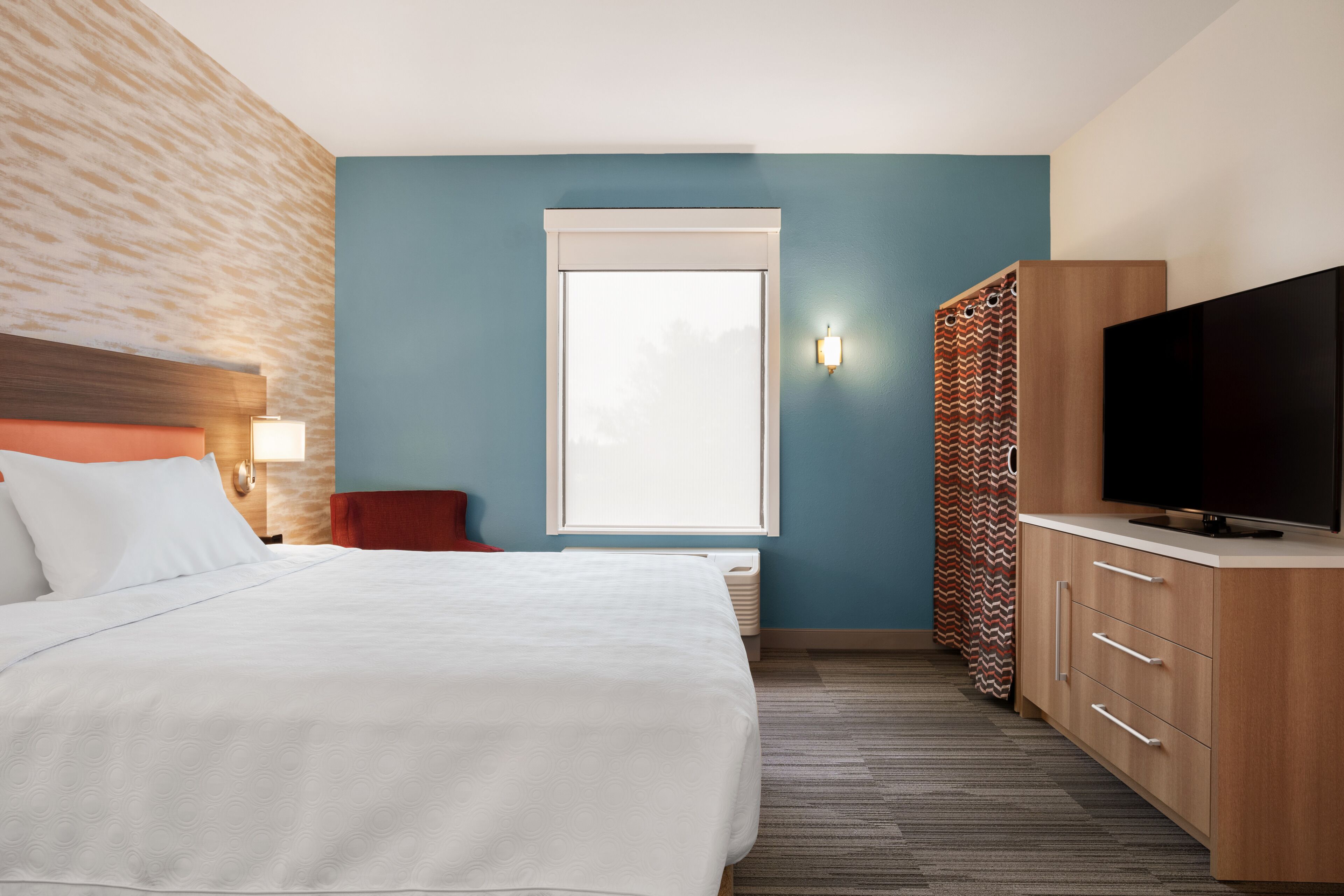 A hotel room with a bed, a TV, a wardrobe, and a window.