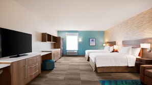A hotel room with a flat-screen TV, a desk with drawers, a bed with white bedding, a nightstand with a lamp, and a large window with a view of the sky. - Home2 Suites by Hilton New Brunswick, NJ (New Brunswick)