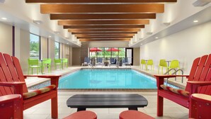 A pool area with red and green chairs, a black table, and a view of the pool through large windows. - Home2 Suites by Hilton New Brunswick, NJ (New Brunswick)