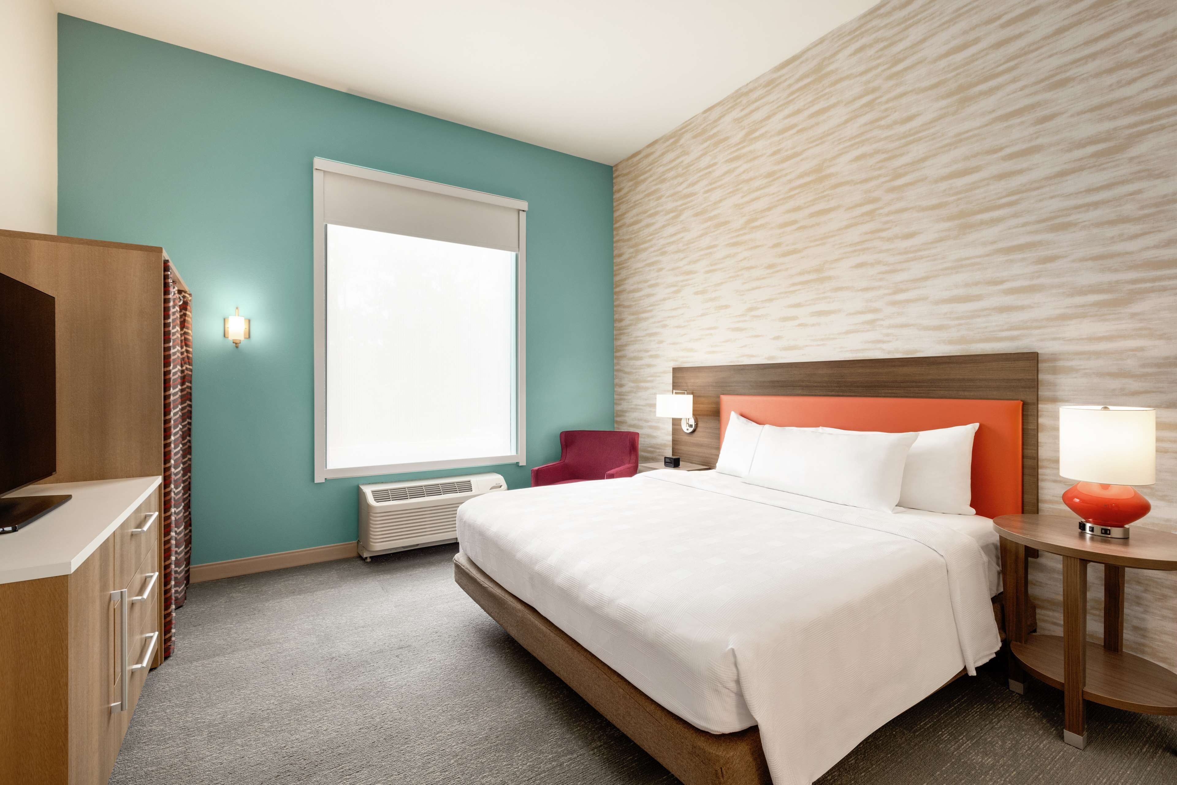 Habitación de hotel con cama, escritorio, silla, ventana y pared con textura.