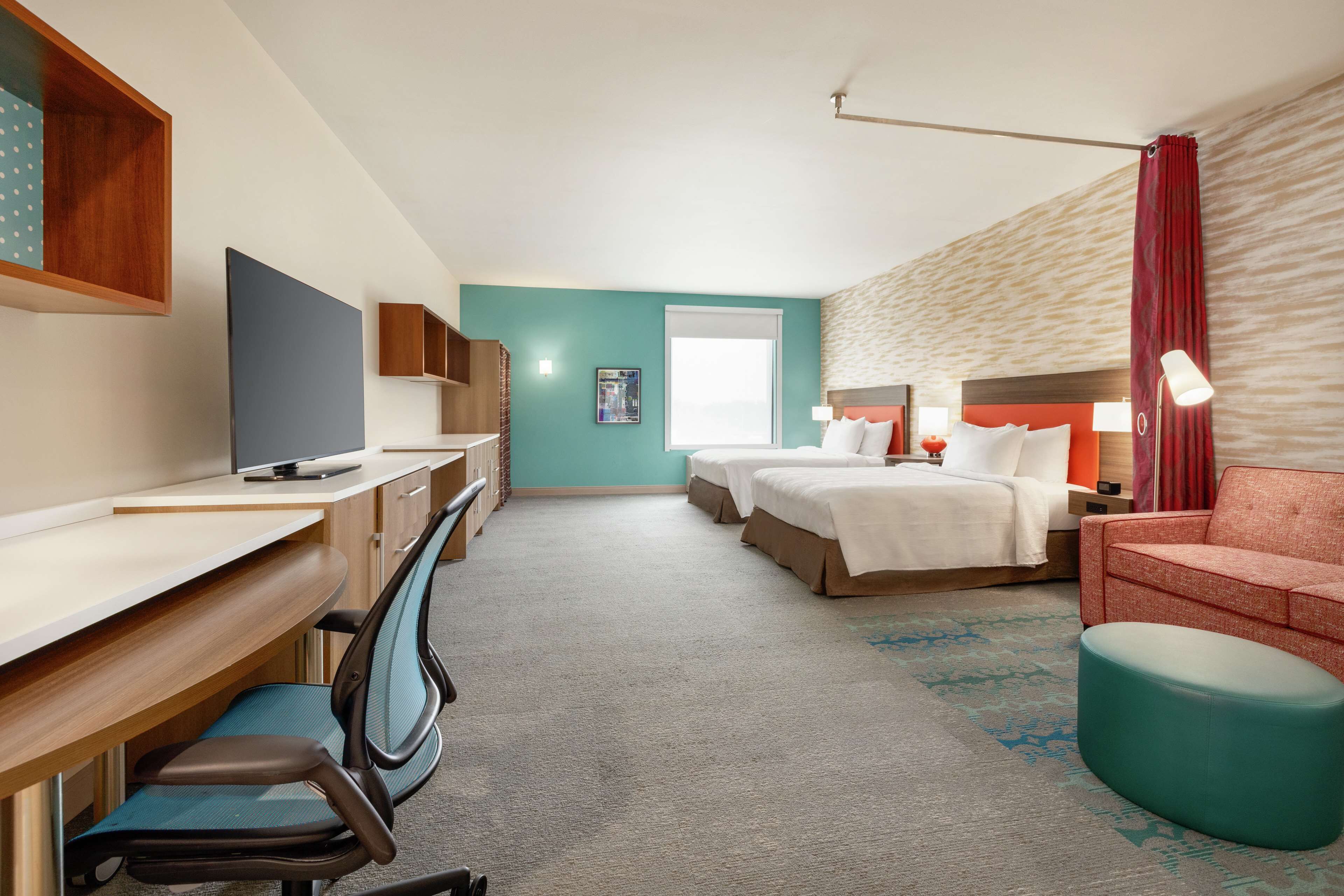 A hotel room with a desk, two beds, a TV, and a red sofa.