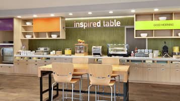 Un café moderno con una mesa y sillas de madera, una barra con diversos productos, y un letrero que dice 'inspired table'.