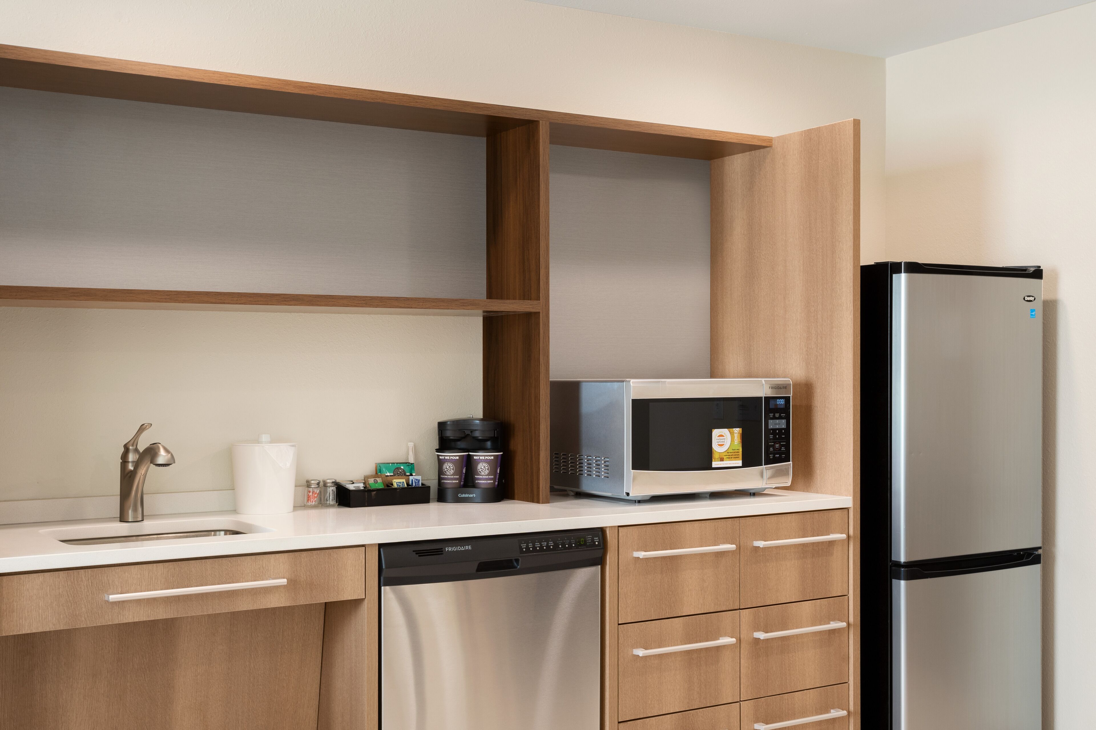 Eine moderne Küche mit einem Edelstahl-Kühlschrank, einer eingebauten Mikrowelle, einem Geschirrspüler und Holzschränken.