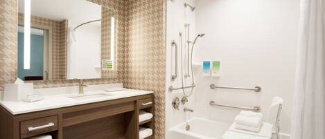 Un bagno moderno con un mobile bagno in legno, un ampio specchio, una vasca da bagno con una sedia a doccia e una barra di sostegno.