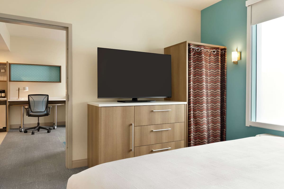 A hotel room with a bed, a desk with a chair, a television on a cabinet, and a window with curtains.