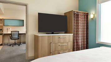 A hotel room with a bed, a desk with a chair, a television on a cabinet, and a window with curtains.