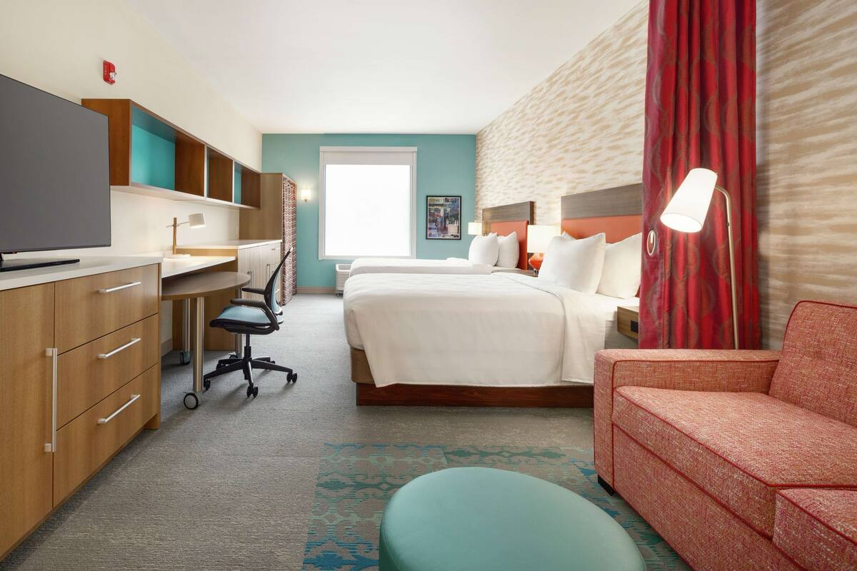 A hotel room with a bed, a desk, a television, a sofa, and a window.
