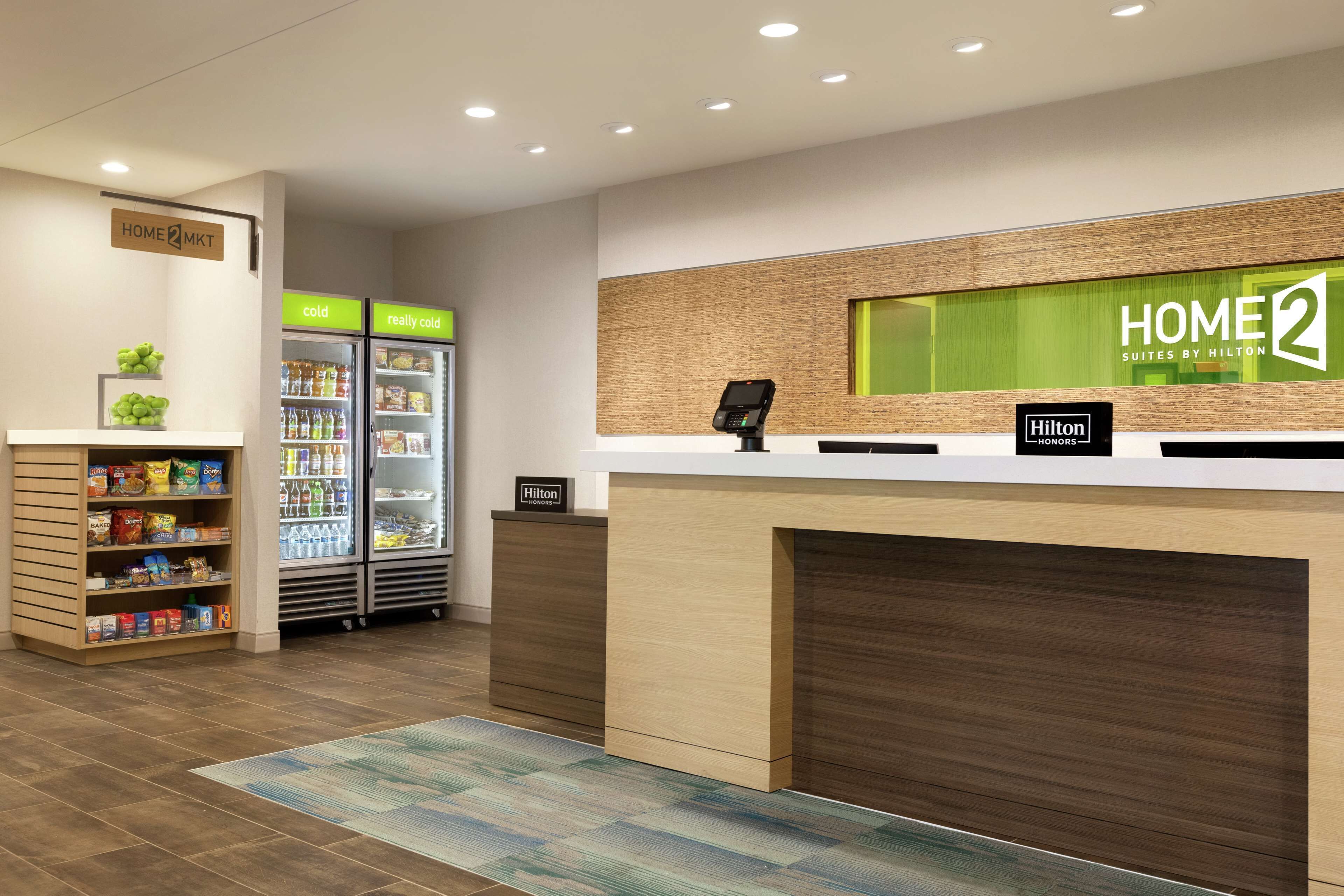 Zona de recepción de un hotel, con mostrador de recepción, un minibar y un refrigerador lleno de bebidas.