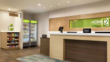 Zona de recepción de un hotel, con mostrador de recepción, un minibar y un refrigerador lleno de bebidas.