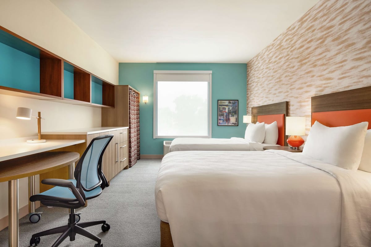 A hotel room with a desk, two beds, a window, and a wall with a textured pattern.