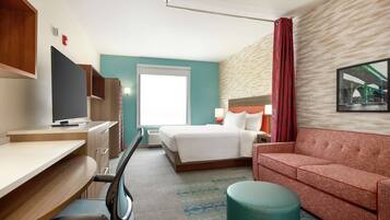 Habitación de hotel con cama, escritorio con computadora, televisor, sofá y ventana con cortinas.
