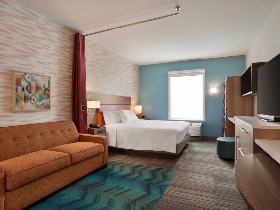 A hotel room with a bed, a sofa, a TV, a desk, and a window.