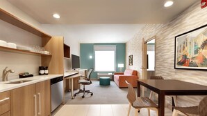 A modern kitchen with wooden cabinets, a dishwasher, and a dining area with a table and chairs. - Home2 Suites by Hilton New Brunswick, NJ (New Brunswick)