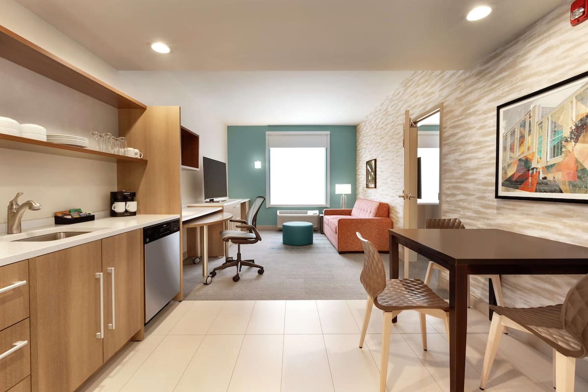 A modern kitchen with wooden cabinets, a dishwasher, and a dining area with a table and chairs.