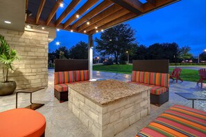 An outdoor patio with a stone fireplace, cushioned seating, and a pergola with string lights. - Home2 Suites by Hilton East Hanover (East Hanover)