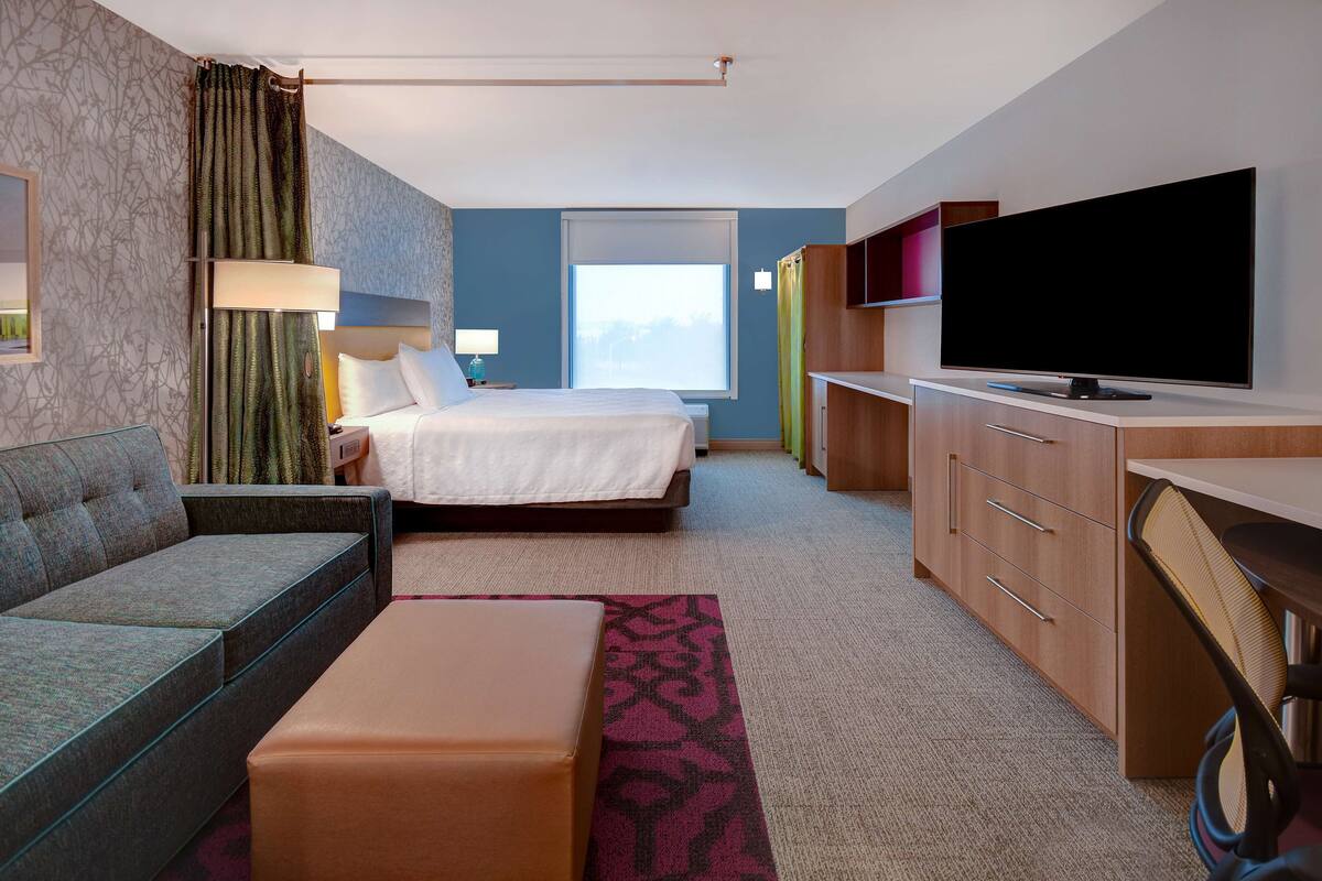 A hotel room with a bed, a sofa, a desk, a television, and a window.