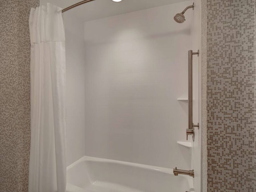 A walk-in shower with a white tiled wall, a showerhead, and a handheld shower attachment.