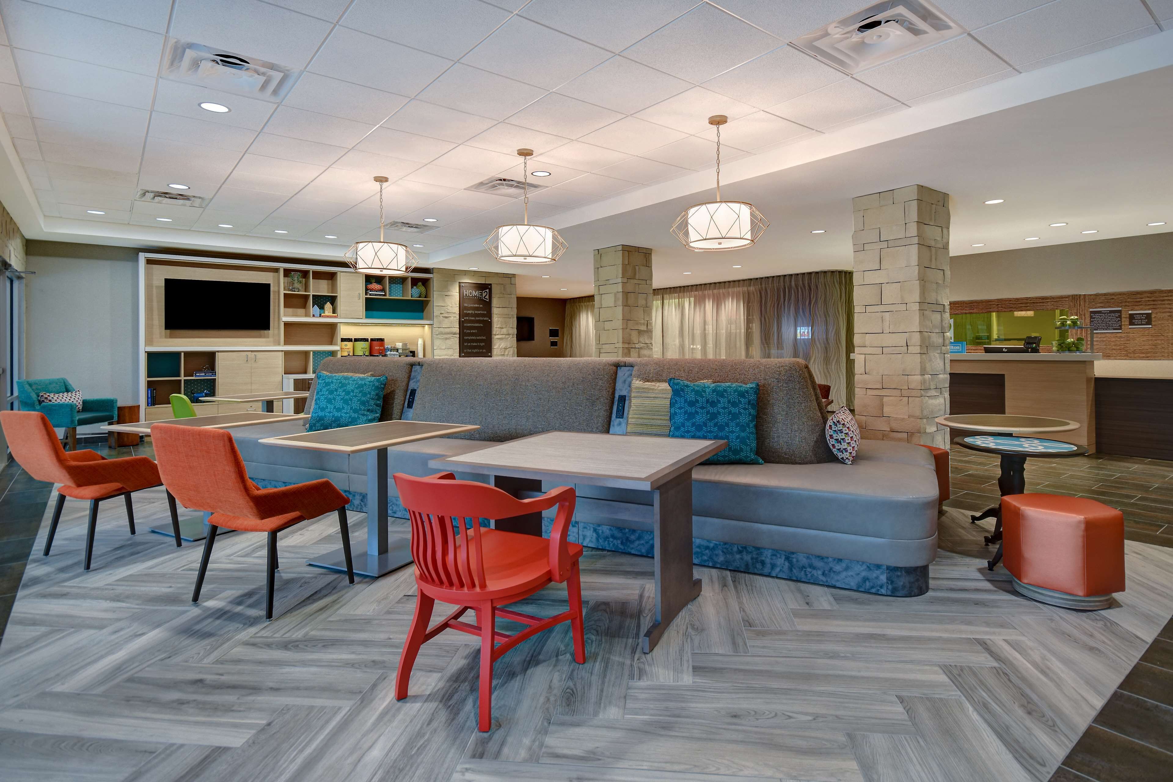 A modern hotel lobby with a seating area, a reception desk, and a TV screen.