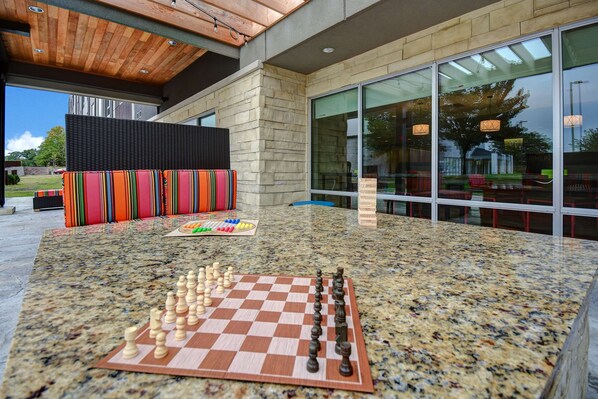 A chessboard set on a granite table in a modern indoor space with a stone wall and large windows. - Home2 Suites by Hilton East Hanover (East Hanover)