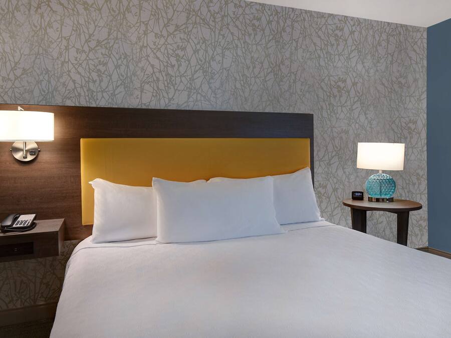 A neatly made bed with white linens, a wooden headboard, and two bedside tables with lamps.