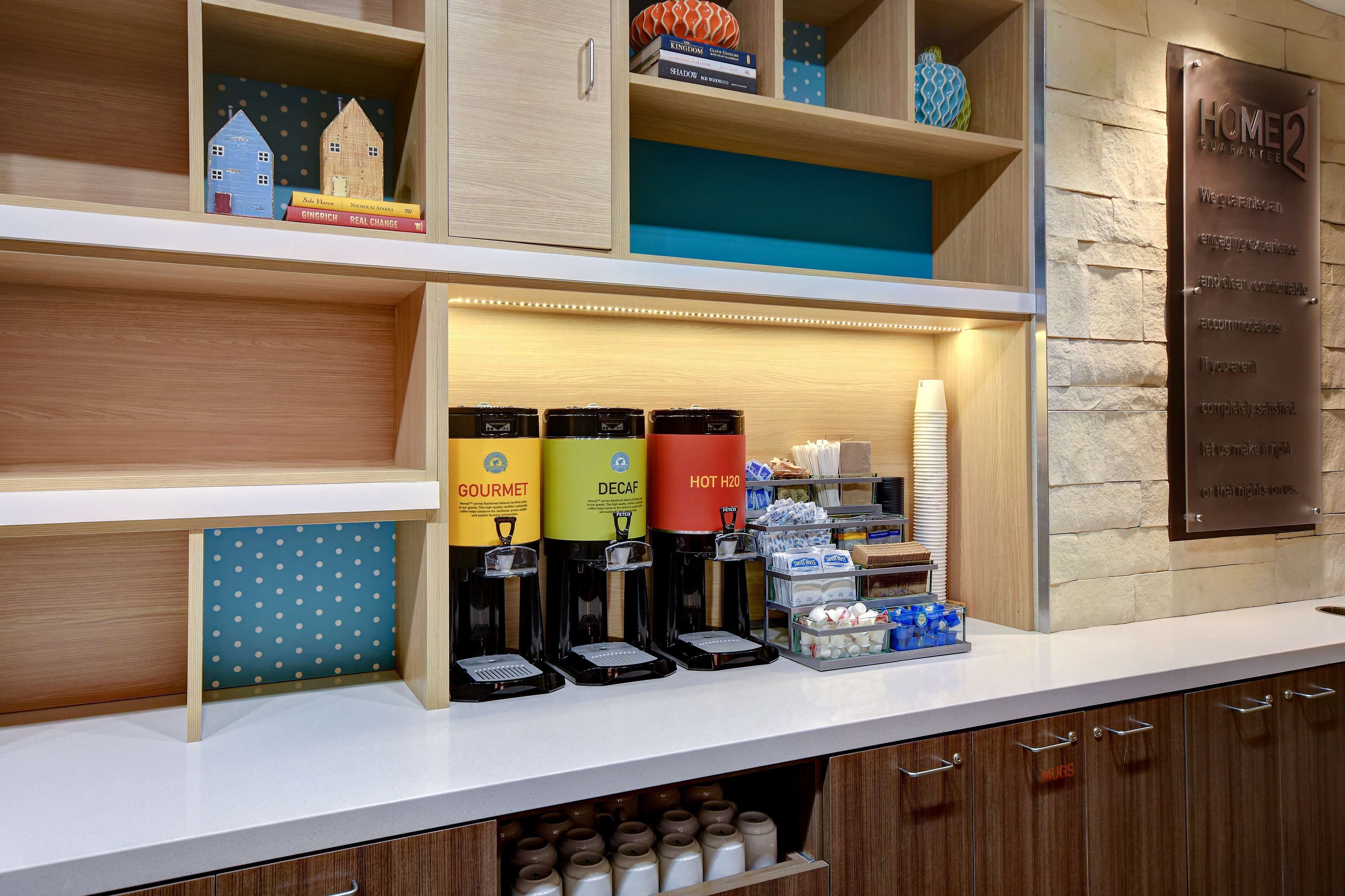 A hotel reception area with a coffee station, books, and a sign indicating amenities.