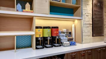 A hotel reception area with a coffee station, books, and a sign indicating amenities.