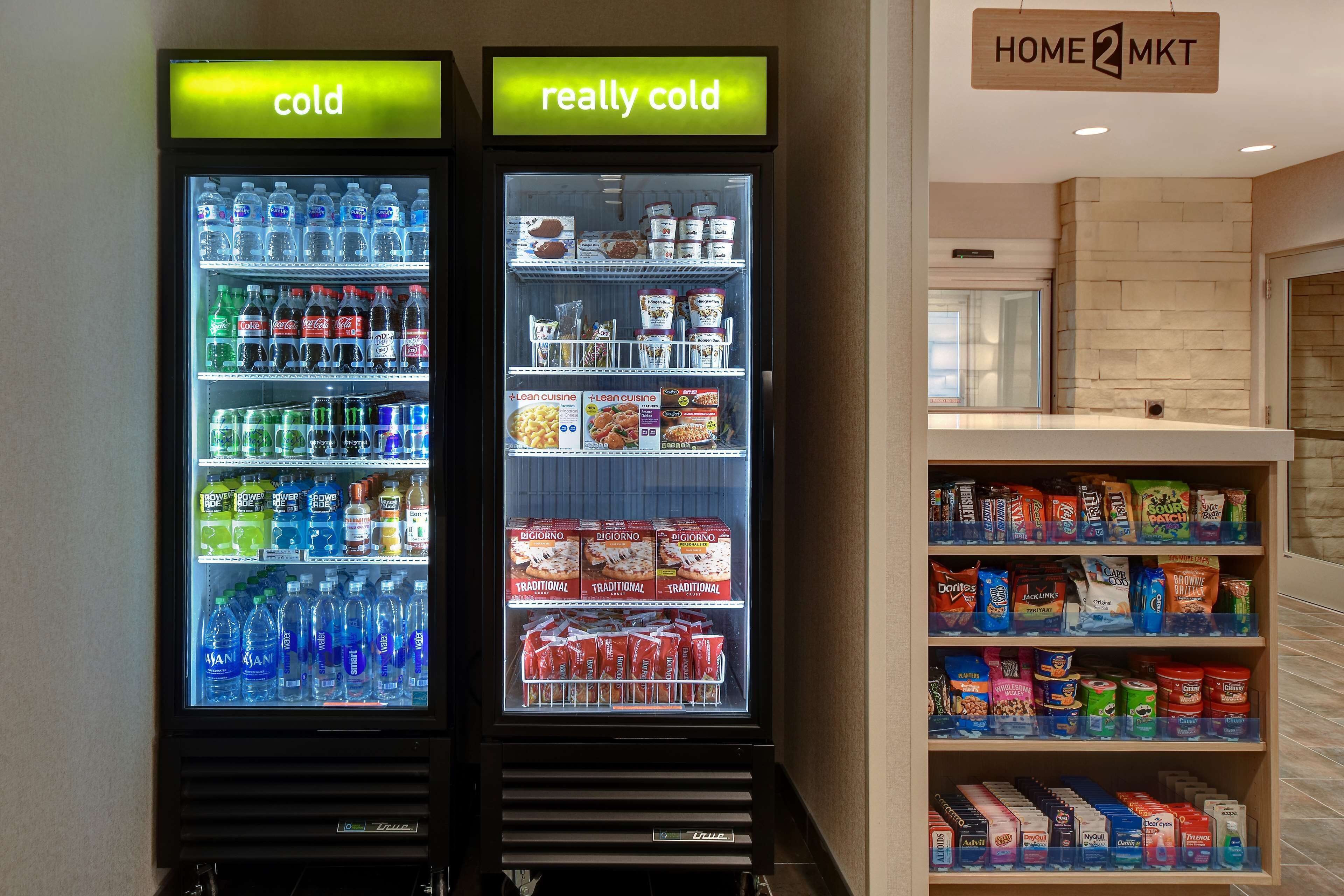 Dos dispensadores refrigerados de bebidas con etiquetas que indican 'frío' y 'muy frío', llenos de varias bebidas y aperitivos.