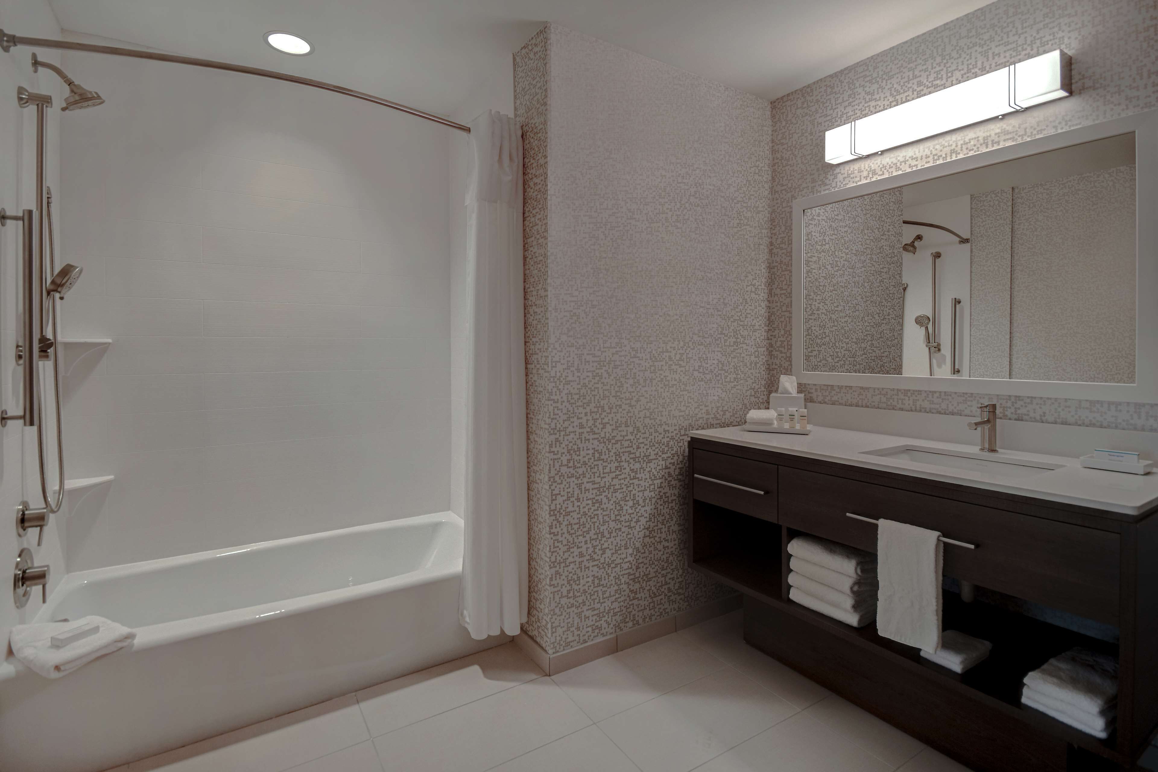 A modern bathroom with a bathtub, a shower, a vanity with a mirror, and a towel rack.